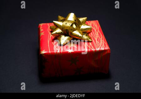 Red square gift box with a golden bow on a black background Stock Photo