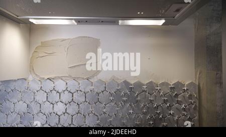 Ceramic tiles glued to the wall. tiles - A man lays a ceramic texture of hexagonal tiles on the wall. Ceramic hexagonal tiles on the wall. Stock Photo