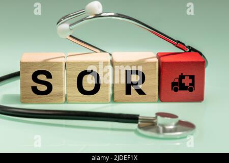 Red Inscription in Polish SOR 'hospital emergency department' on wooden blocks, a medical stethoscope and an ambulance symbol, Health concept in Polan Stock Photo