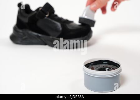 A person applies sponge paint cream to the black crumbs of the child. Care for children's leather and suede shoes. Stock Photo