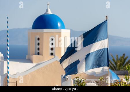 Medium close-up shot of a blue church dome with the old greek national flag in the foreground Stock Photo