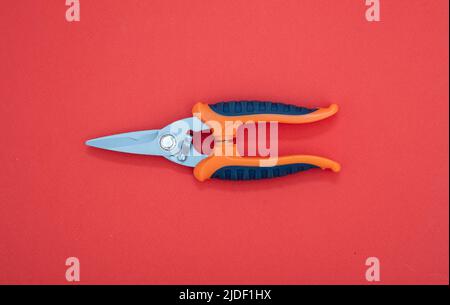 Sheet metal shears with steel point, orange, blue color rubber handle on red background. Hand tool, new scissors with sharp blade, metalwork implement Stock Photo