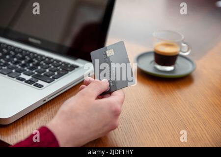 Hands holding plastic credit card and using laptop, wooden table background, close up view. Online shopping concept Stock Photo