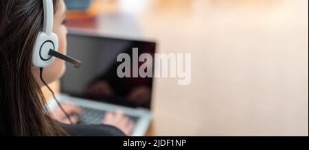 Customer support, help desk call center concept. Woman with headset working with a laptop, talking on phone, view from behind. Copy space Stock Photo
