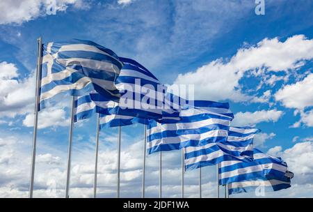 Greece sign symbol, cloudy blue sky, sunny spring day in Athens. Greek national official flags on flagpoles in a row waving in the wind. Stock Photo