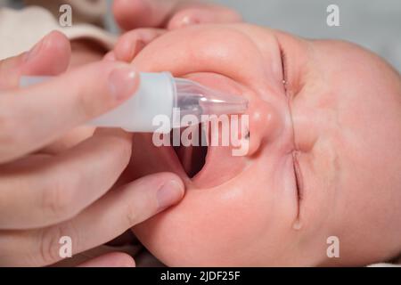 Mother removes snot of newborn baby using nasal aspirator Stock Photo