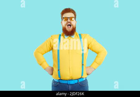 Funny bearded chubby man laughing loudly holding his hands to his sides on light blue background. Stock Photo
