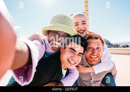 Group of friends giving piggyback ride to girlfriends. Happy young friends enjoying a weekend day. Stock Photo