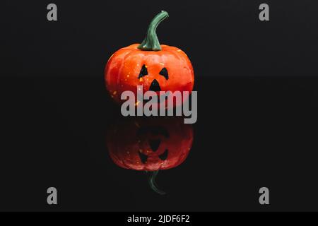 Halloween pumpkin with typical face isolated on black reflective surface. Background is dark. Stock Photo