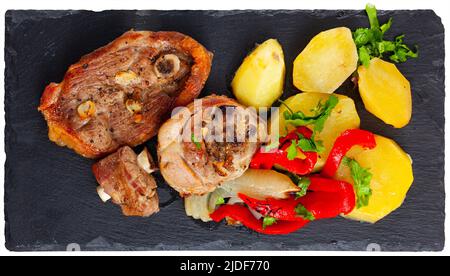 Fried lamb leg steaks with potatoes, red pepper slices, greens on slate board Stock Photo