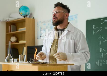 Confident mature male teacher of chemistry making report about chemical reactions while standing by desk in front of audience Stock Photo