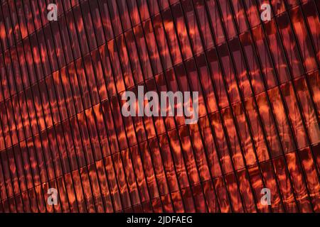 The glass and iron facade of huge skyscraper at sunset, steel, orange color, reflection of sun Stock Photo