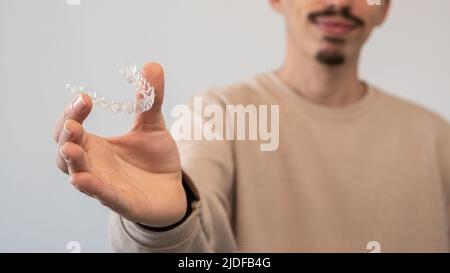 Adult man holds invisalign transparent braces for dental correction. Caucasian person holding invisible orthodontic retainer and aligner. Plastic brac Stock Photo