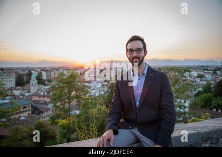 Young smiling caucasian businessman sitting on terrace during break time with sunset on background. Stock Photo