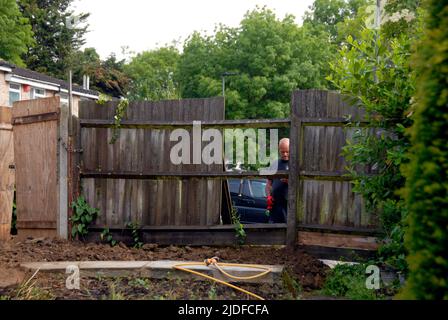 Workman starting to take apart old domestic garden fence before replacing it with a new fence Stock Photo