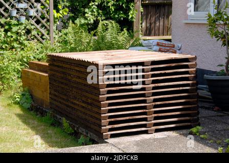 Stack of wooden fence panels, posts, gravel boards and cement mix, stored on patio ready for replacing old domestic garden fence Stock Photo