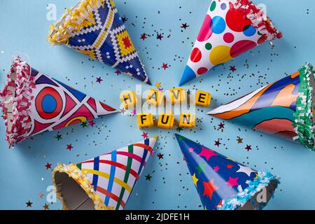 Various birthday cones with confetti on blue background. Yellow letter cubes with have fun message. Stock Photo