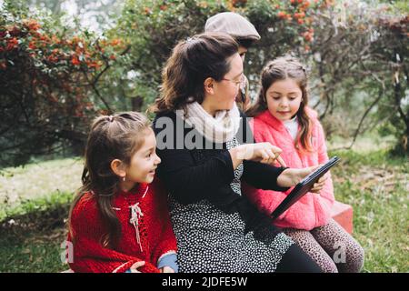 Single mother with her son and daughters using a tablet to watch a movie, in the park. Latin single parent family Stock Photo