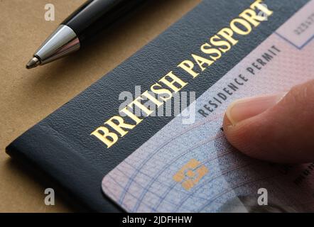 Finger pointing at Biometric Residence permit Card (ILR, Indefinite leave to Remain) placed on top of British passport. Concept for naturalisation. Stock Photo