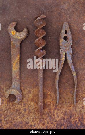 Rusty old double-headed spanner lying next to large drill bit and rusty pliers on rusty metal sheet Stock Photo