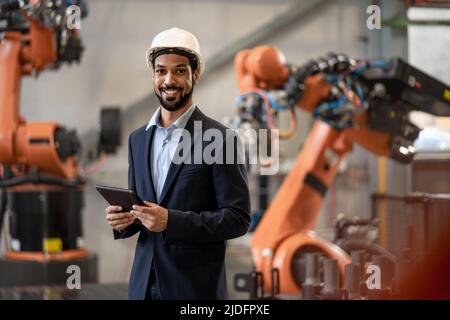 Automation engineer uses tablet for programming robotic arm in factory. Stock Photo
