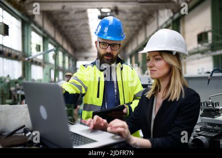 Male and female industrial engineers discussing factory's new machinery project and using laptop. Stock Photo