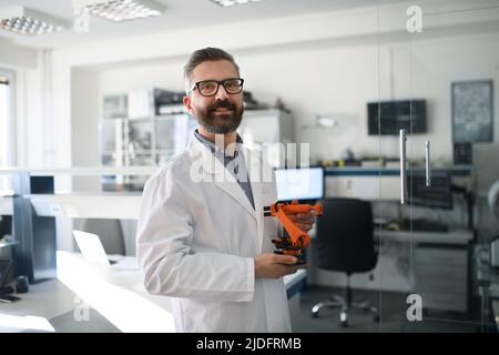 Robotics engineer holding modern robotic arm, standing and looking at camera in laboratory office. Stock Photo