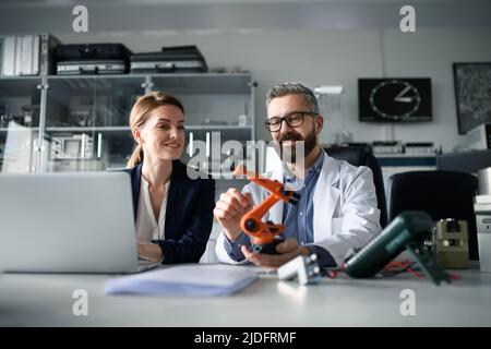 Robotics engineers working on laptop and desinging modern robotic arm in laboratory. Stock Photo