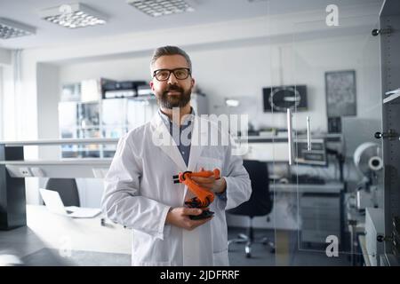 Robotics engineer holding modern robotic arm, standing and looking at camera in laboratory office. Stock Photo