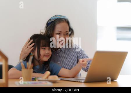 Happy moments of Asian grandmother with her granddaughter using video call. Leisure activities for children at home. Stock Photo