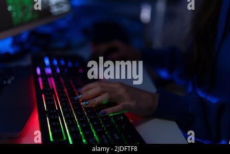 Close-up of woman hacker hands at keyboard computer in the dark room at night, cyberwar concept. Side view. Stock Photo