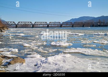Fraser River Rail Bridge Winter BC. A rail bridge crossing the Fraser River with floating ice in the winter. Mission, British Columbia, Canada. Stock Photo