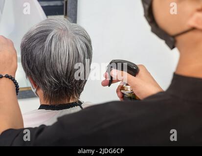 Man hairdresser cuts senior woman's hair with scissors Stock Photo