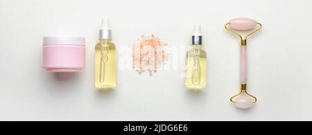 Essential oil, jar of cosmetic cream, sea salt and facial massage tool on white background Stock Photo