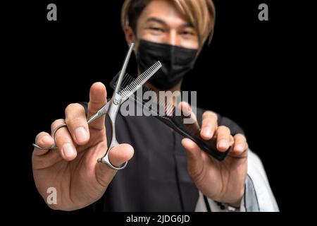 Portrait of hairdresser with scissors and comb in hands isolated on black background Stock Photo