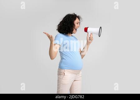 Young pregnant woman shouting into megaphone on light background Stock Photo