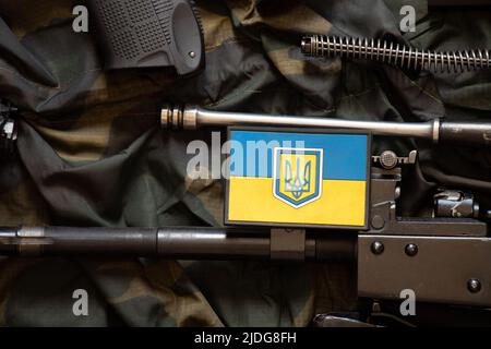 The patch of the flag of Ukraine lies on a disassembled machine gun on a green camouflage fabric, war in Ukraine Stock Photo