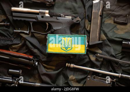 The patch of the flag of Ukraine lies on a disassembled machine gun on a green camouflage fabric, war in Ukraine Stock Photo