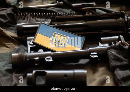 The patch of the flag of Ukraine lies on a disassembled machine gun on a green camouflage fabric, war in Ukraine Stock Photo