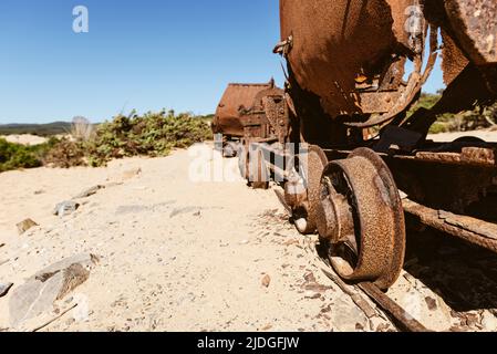Rusty broken wagons and scrap of a railway from the lead and zinc mines to the sand dunes near the beach of Piscinas, Costa Verde, Sardinia, Italy Stock Photo