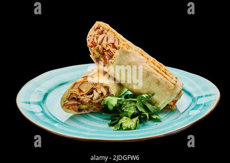 Shawarma of chicken in garlic lavash lies on a plate on a black isolated background Stock Photo