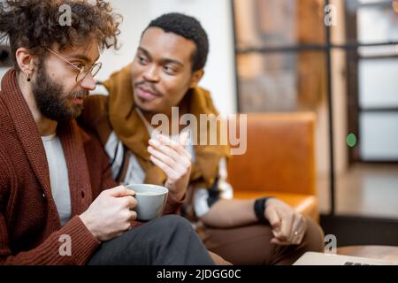 Male gay couple talking on a couch at home Stock Photo
