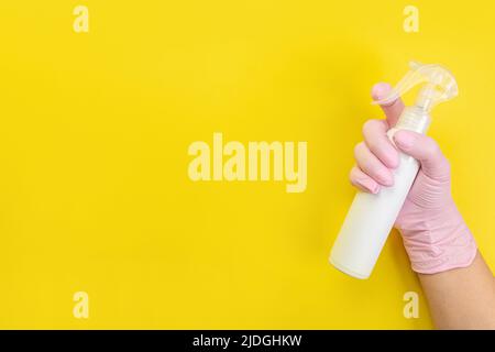 Close up of female hand in pink gloves holds  bottle with cleaner liquid for washing dishes with place for text on yellow background. Cleaning supplie Stock Photo