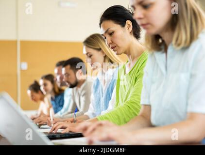 Woman university student sitting at table and handwriting, using laptop Stock Photo