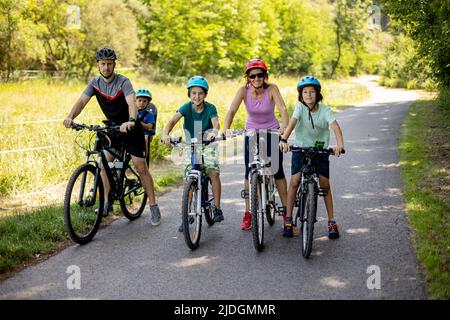 Happy family, parents and children, riding bikes in the park on a sunny summer day, enjoying quality family time together Stock Photo