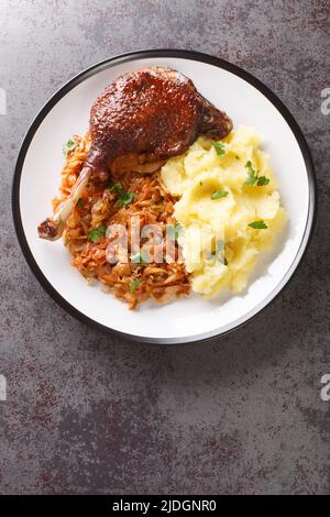 Romanian Rata pe varza duck leg serving with mashed potatoes and stewed cabbage close-up in a plate on the table. Vertical top view from above Stock Photo