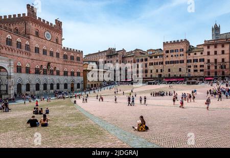 Siena, Italy - May 29 2018: People enjoy a sunny day in Piazza del Campo, one of Europe's greatest medieval squares. Palazzo Pubblico is on the left. Stock Photo