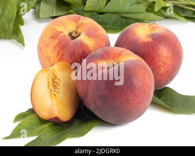 Peaches with slice and leaves isolated on bright background. Close up view. Stock Photo