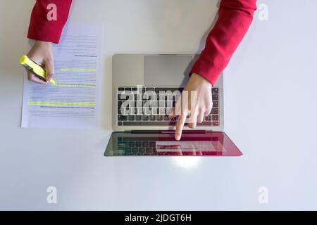 Holding highlighter pen, top view of woman hand holding highlighter pen. Working on laptop and highlighting or marking important text on working paper Stock Photo