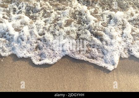 Close up photo of waves hitting the beach by creating bubbles. Stock Photo